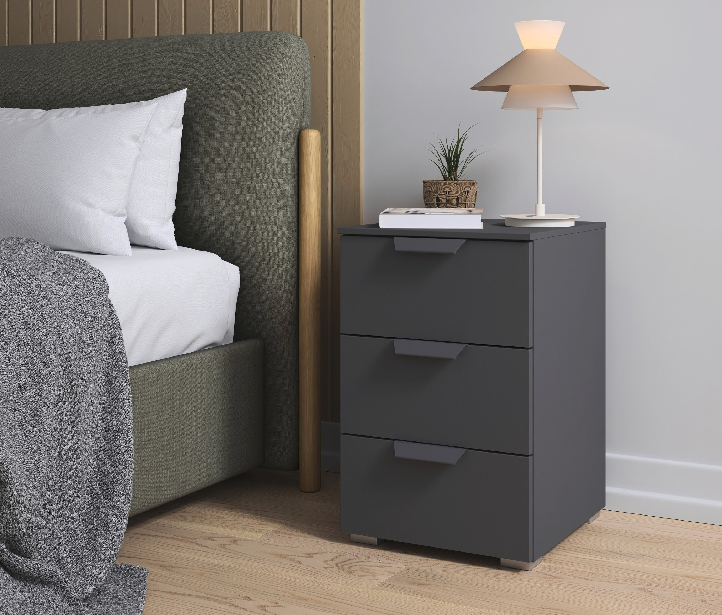 Ein grauer rauch Nachttisch »Holga« steht neben einem Bett mit grauer Decke und weißem Kissen.