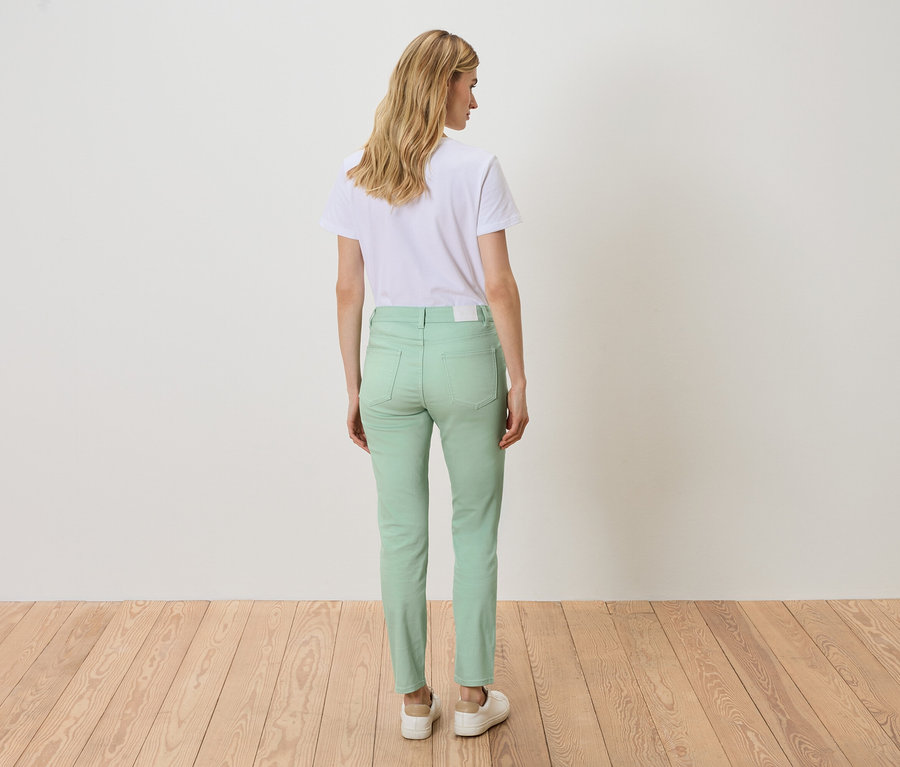 Rückansicht einer blonden Frau in einem weißen T-Shirt und hellgrünen Jeans.