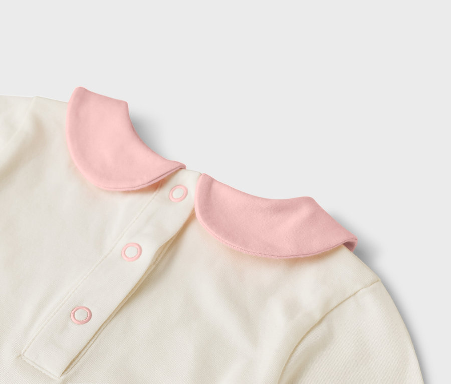 Detailansicht eines cremefarbenen Oberteils mit rosa Kragen und Knöpfen.