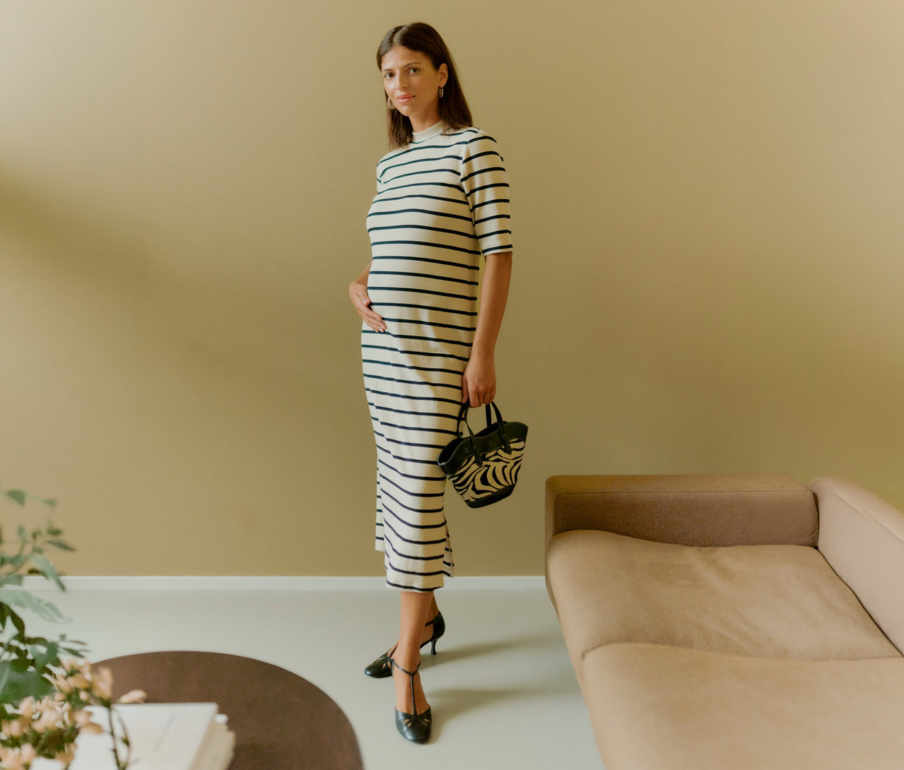 Frau im gestreiften MAMALICIOUS Kleid »MLLANE« mit Hand auf dem Bauch, hält eine Handtasche. Sie trägt schwarze Schuhe.