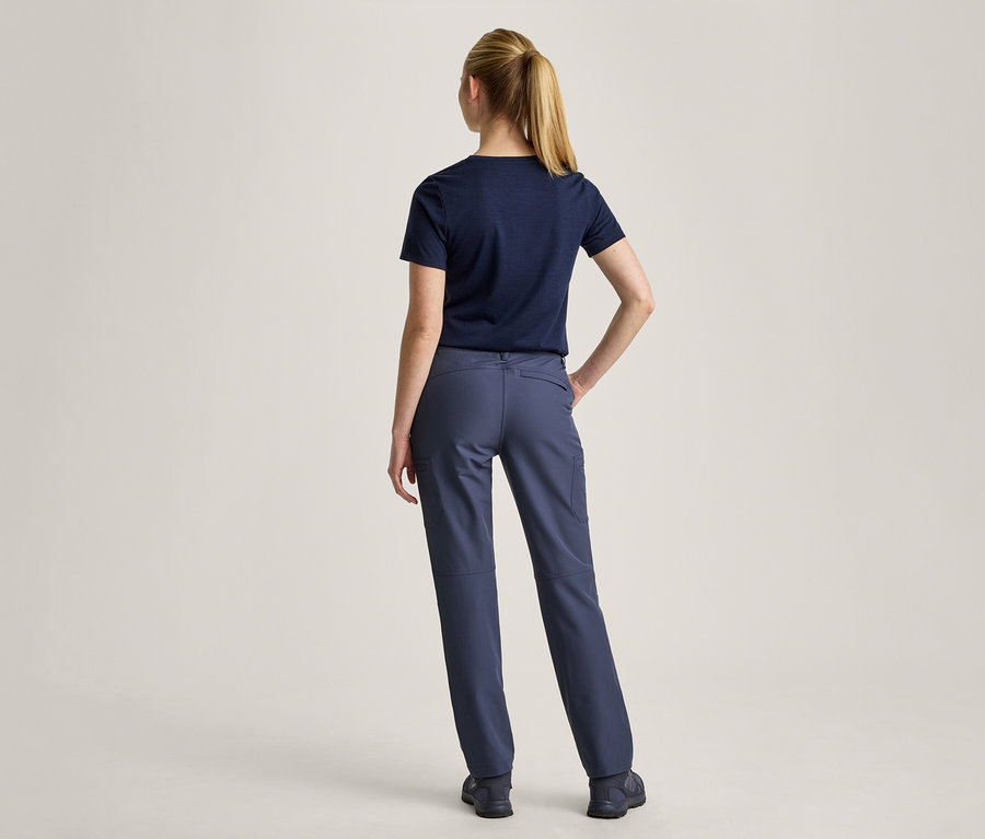 Frau von hinten, die ein dunkelblaues T-Shirt und eine dunkelblaue Hose trägt. Sie hat die Haare zu einem Pferdeschwanz gebunden und die linke Hand in die Hüfte gestemmt.