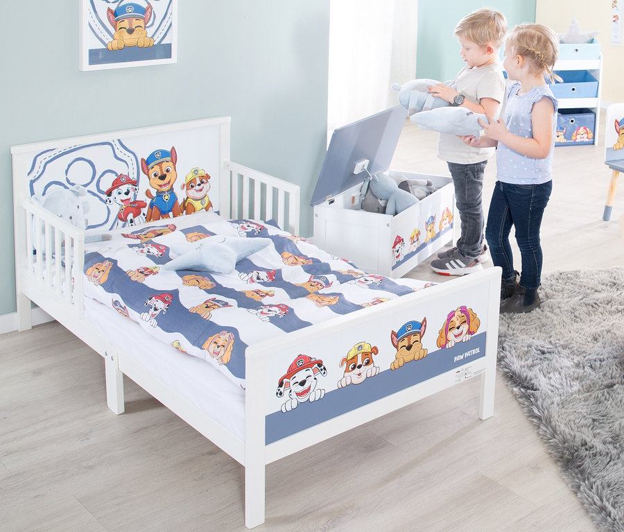 Zwei Kinder räumen Spielzeug in eine Spielzeugkiste neben einem Paw Patrol Kinderbett.