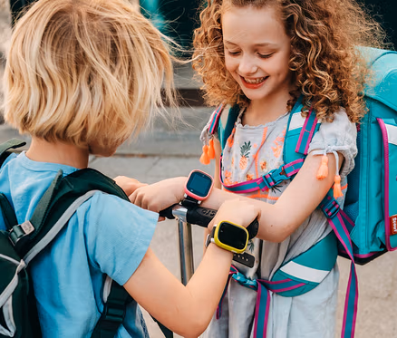Zwei Kinder liegen in einem grünen Zelt auf einer Wiese. Der Junge links trägt eine braune Kappe und eine Uhr am Handgelenk. Das Mädchen rechts hat lockiges Haar. Der Junge trägt eine Kids Watch Xplora X6Play