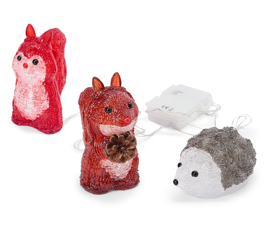 Zwei rote, durchscheinende Eichhörnchen-Figuren und ein weiß-grauer, durchscheinender Igel, die über dünne Drähte mit einem weißen Batteriefach verbunden sind. Ein Eichhörnchen hält einen Tannenzapfen.