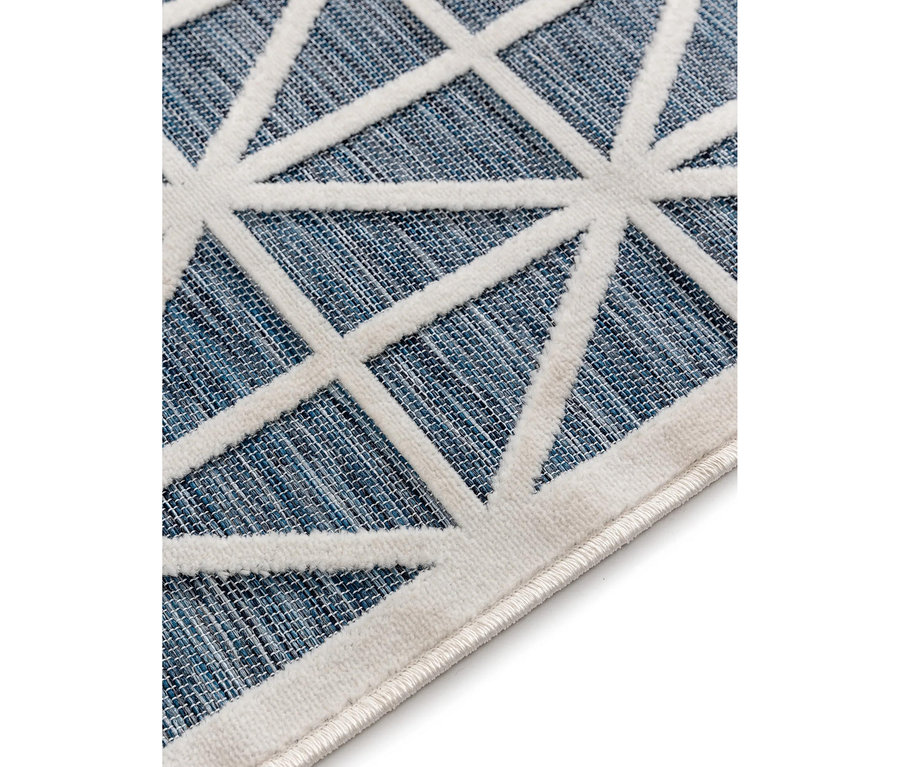 Nahaufnahme eines Teppichs mit blauem, gewebtem Hintergrund und erhabenem, weißem geometrischem Muster aus Dreiecken und Linien.
