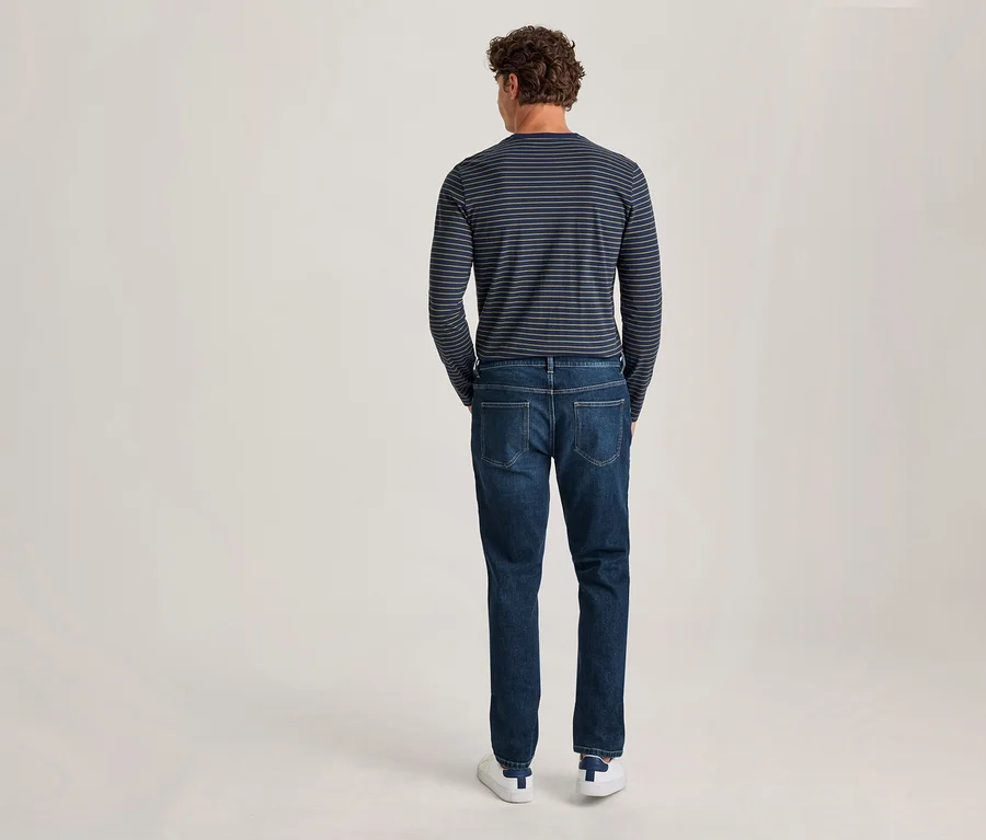 Mann von hinten, trägt ein dunkelblau-weiß gestreiftes Langarmshirt, dunkelblaue Jeans und weiße Sneaker.