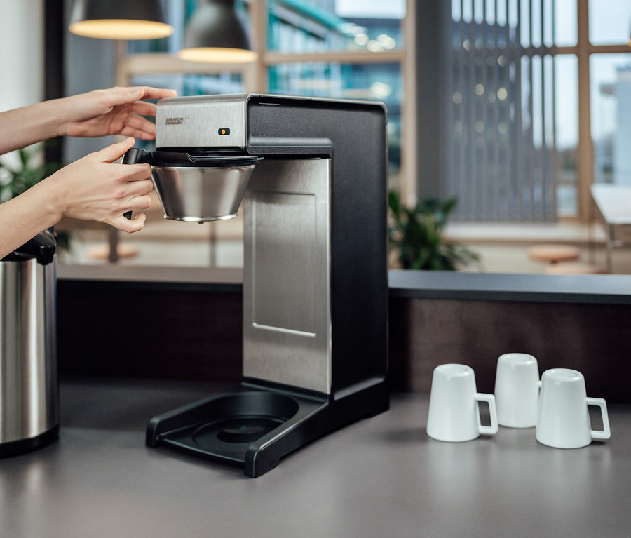 Frau setzt Filter in Profi-Filterkaffeemaschine »Bravilor-Bonamat TH« ein. Auf der Theke stehen eine Thermoskanne und drei weiße Tassen.