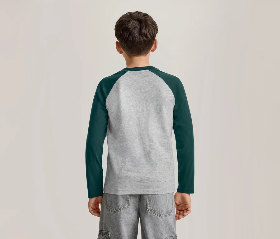 Ein kleiner Junge von hinten, der ein langärmeliges Raglan-T-Shirt in Grau und Dunkelgrün sowie graue Shorts trägt.