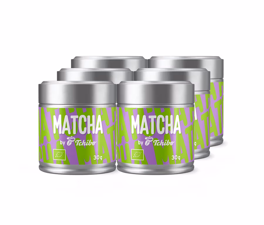 Sechs silberne Dosen Tchibo Matcha Tee mit grün-violetten Etiketten, auf denen „MATCHA by Tchibo“ und „30g“ sowie ein Bio-Logo zu sehen sind.