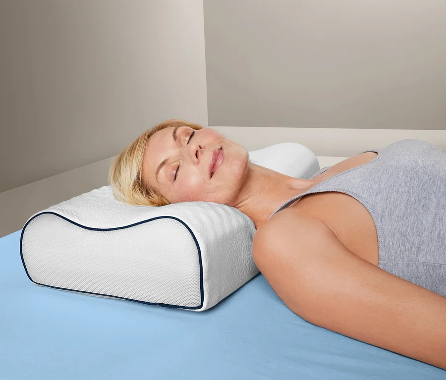 Frau liegt seitlich auf einem blauen Bett und auf einem irisette® Nackenstützkissen.
