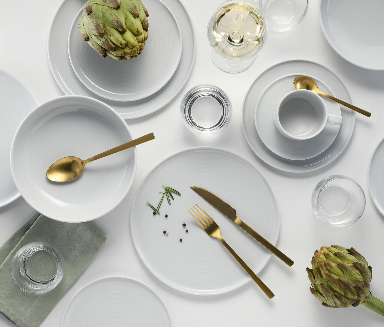 Gedeckter Tisch mit weißem creaTable Service »Session White«, 30-teilig, goldenem Besteck und Gläsern. Zwei Artischocken auf Tellern.