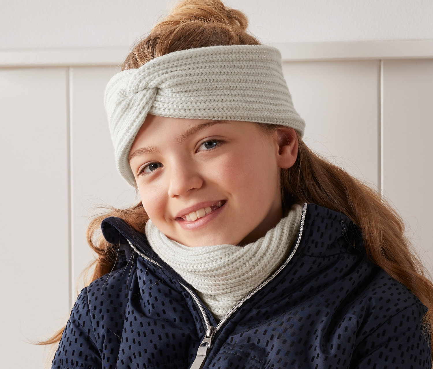Lächelndes Mädchen trägt ein Strickstirnband mit Knotendetail.