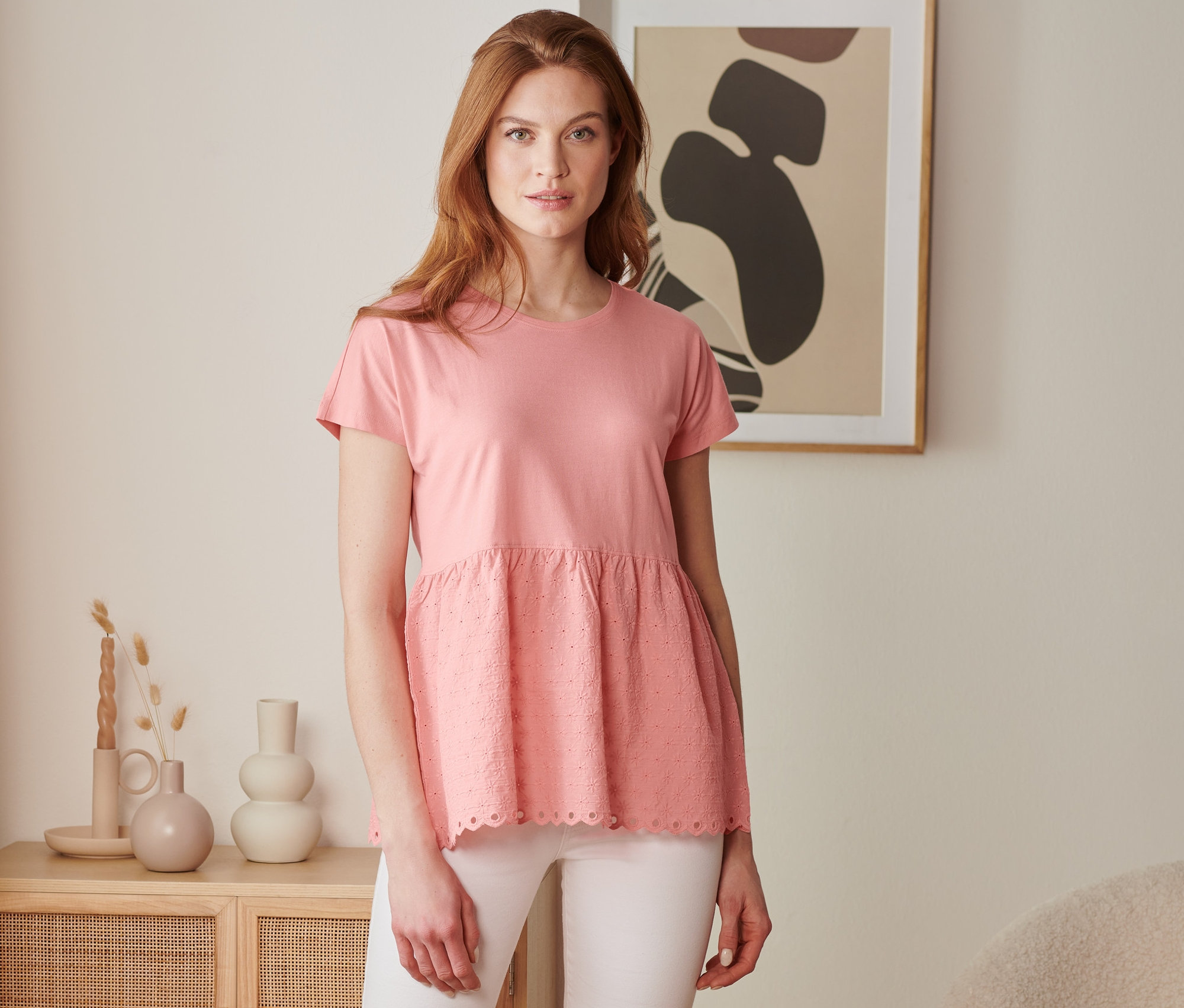 Frau trägt ein korallefarbenes Shirt im Materialmix mit Stickerei und weiße Hose.