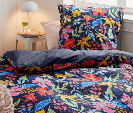 Bett mit blumengemusterter Perkal-Bettwäsche, einschließlich Doppel-, Normal- und Übergrößen. Auf dem Nachttisch steht eine Lampe.