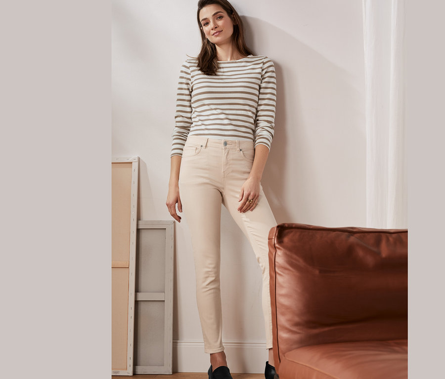Eine Frau posiert in einem beige-weiß gestreiften Langarmshirt aus Bio-Baumwolle und einer Skinny Jeans.