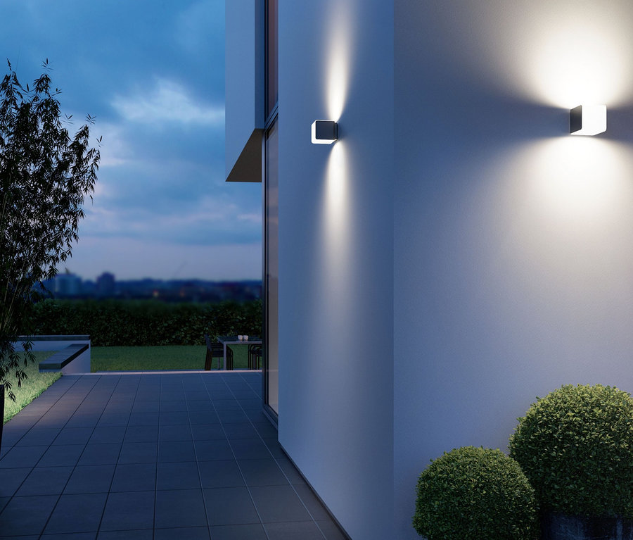 Zwei anthrazitfarbene Steinel Sensor Wandleuchten »L830« beleuchten die Wand eines Gebäudes neben einer Terrasse.