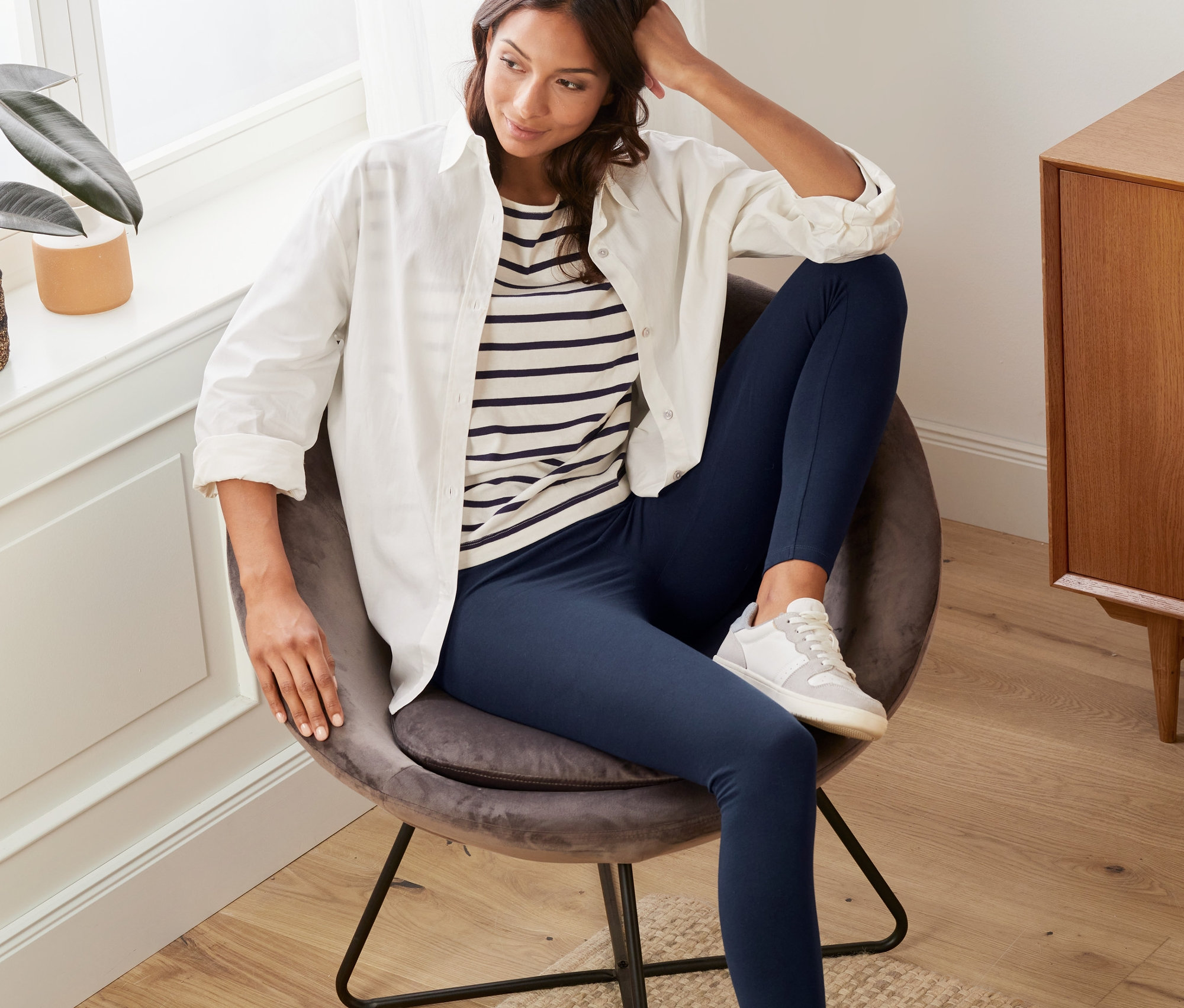 Frau sitzt im Sessel und trägt dunkelblaue Leggings.