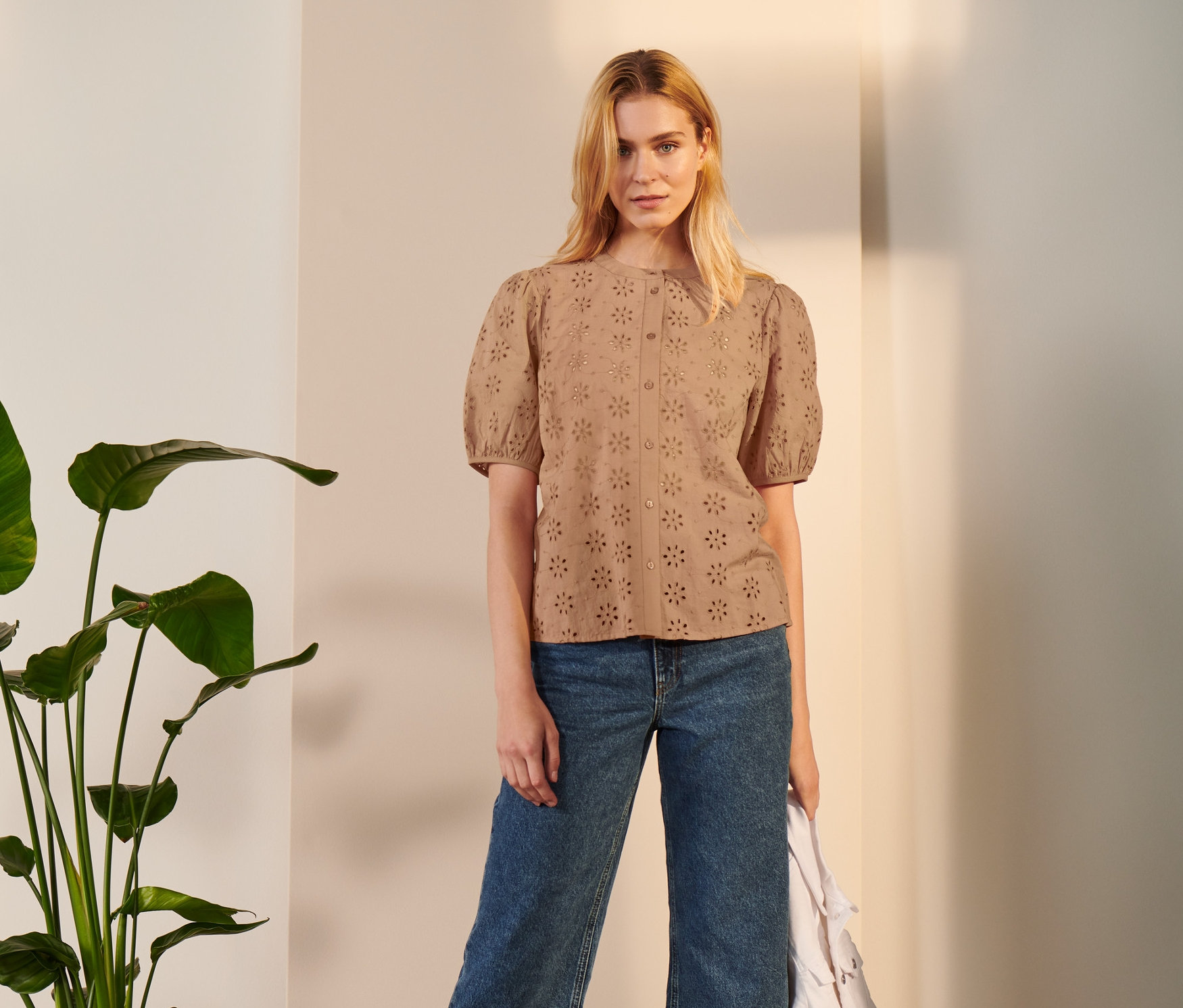 Frau posiert in Lochstickerei Bluse, Jeans und Sandalen.