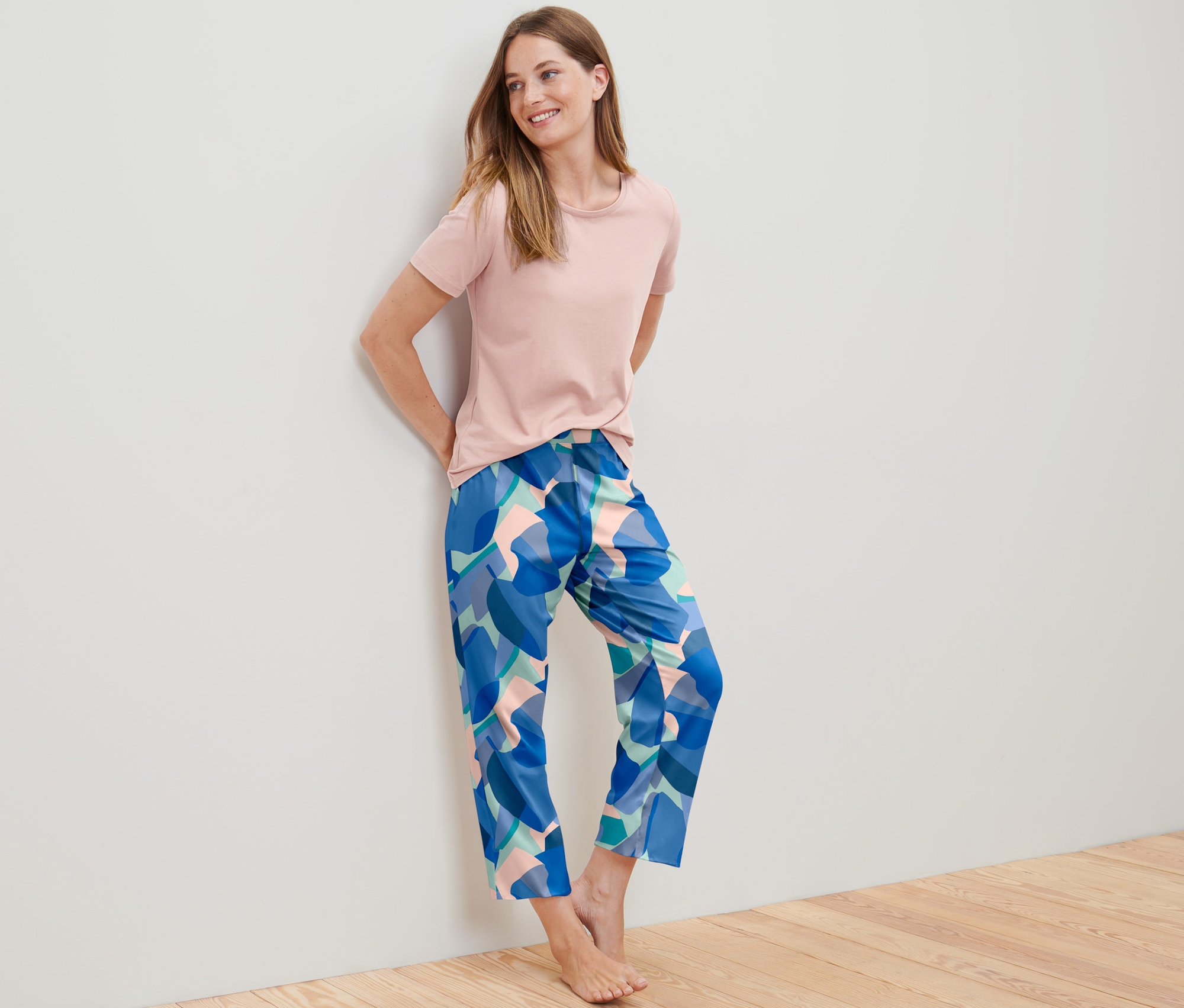 Frau lehnt in einem Pyjama an einer Wand.