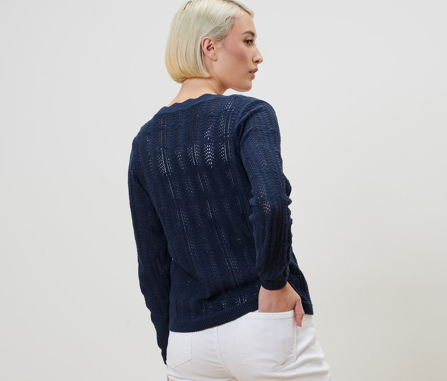 Frau steht mit dem Rücken zur Kamera und trägt eine Strickjacke mit Ajour-Muster und weiße Jeans.