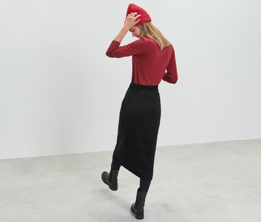 Frau richtet rote Strickmütze. Sie trägt ein rotes Oberteil und einen schwarzen Strickrock.