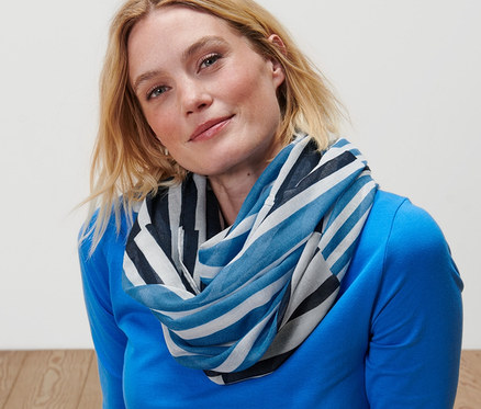 Blonde Frau sitzt auf dem Boden und trägt einen gestreiften Loop-Schal.