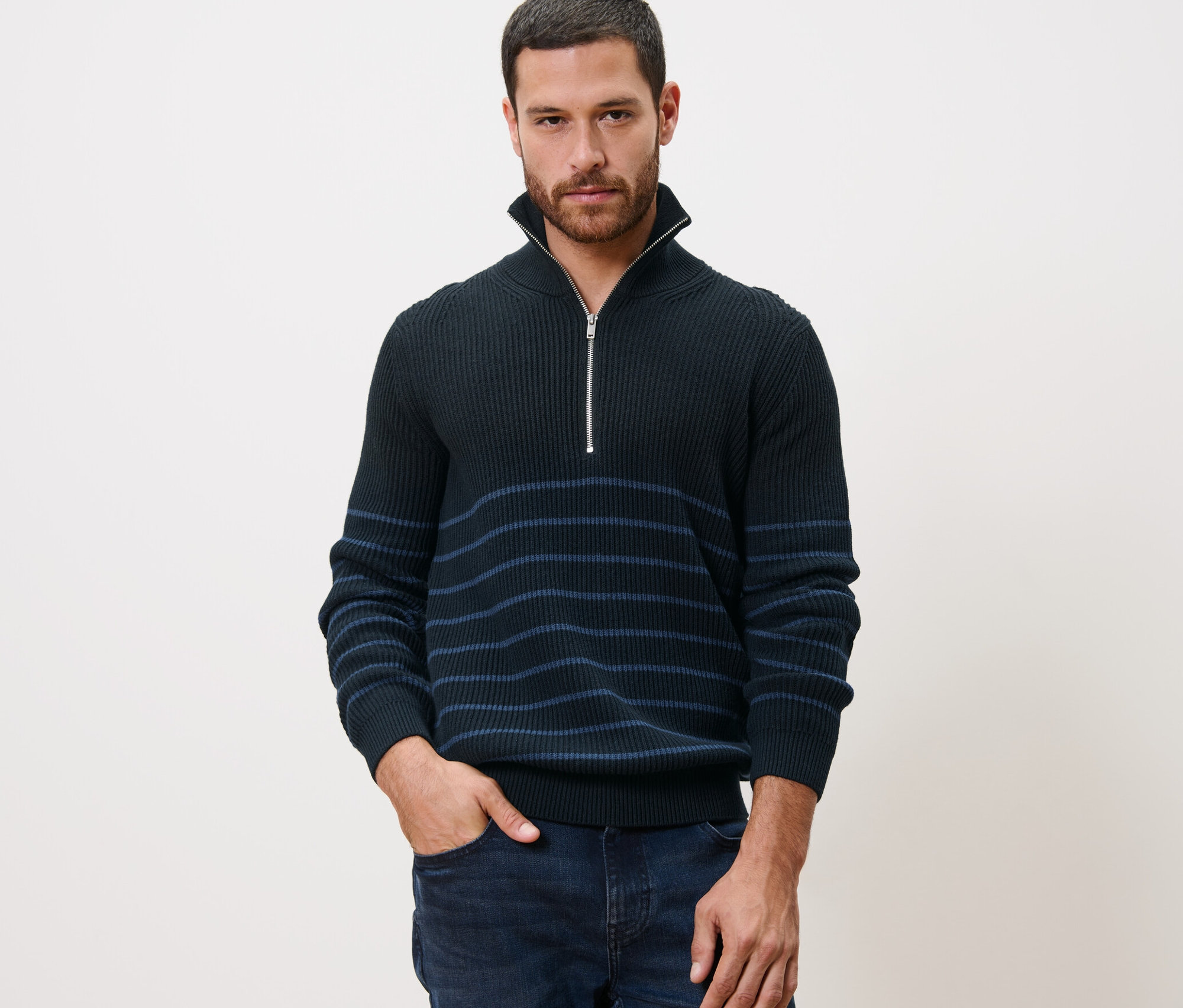 Mann posiert in Troyer-Pullover mit der Hand in der Hosentasche.