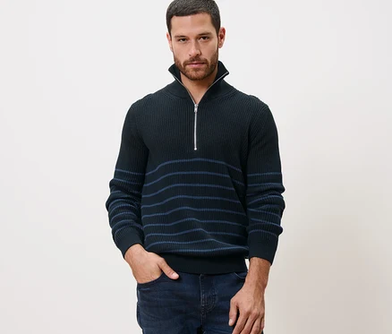 Mann posiert in Troyer-Pullover mit der Hand in der Hosentasche.