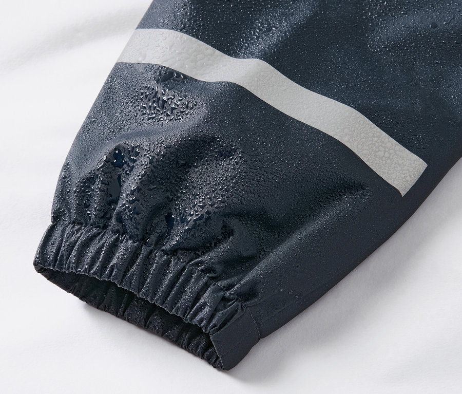Detailaufnahme vom Ärmel einer dunkelblauen Kinder-Regenhose mit Reflexstreifen und Wassertropfen.