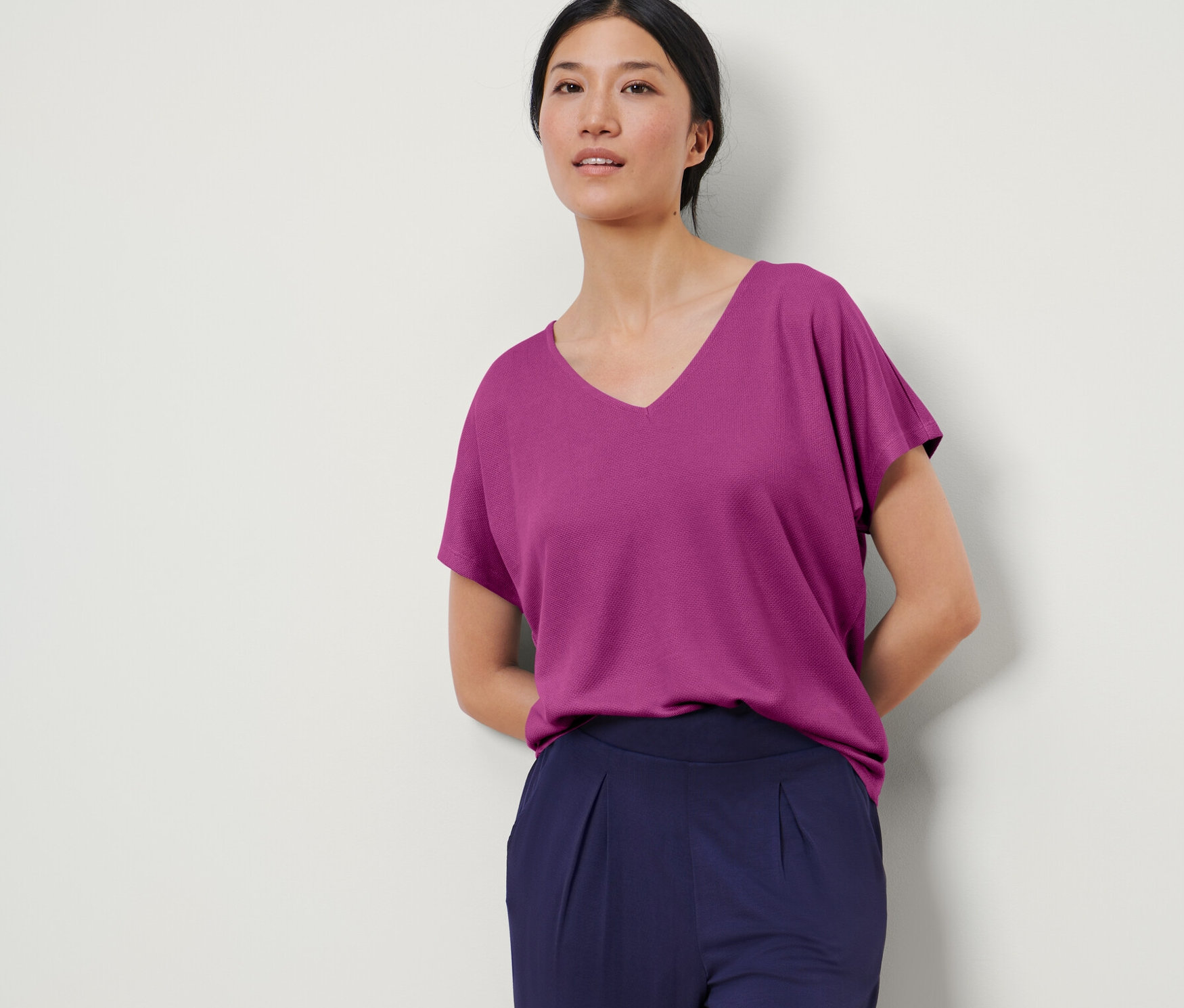 Frau posiert in einem strukturierten Shirt in Berry-Farbe und dunkelblauen Hosen.