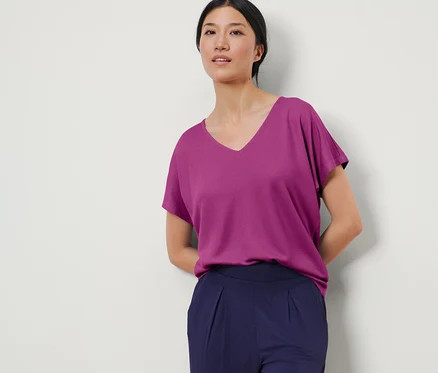 Frau posiert in einem strukturierten Shirt in Berry-Farbe und dunkelblauen Hosen.