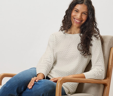 Frau sitzt im Sessel und trägt einen Struktur-Strickpullover.