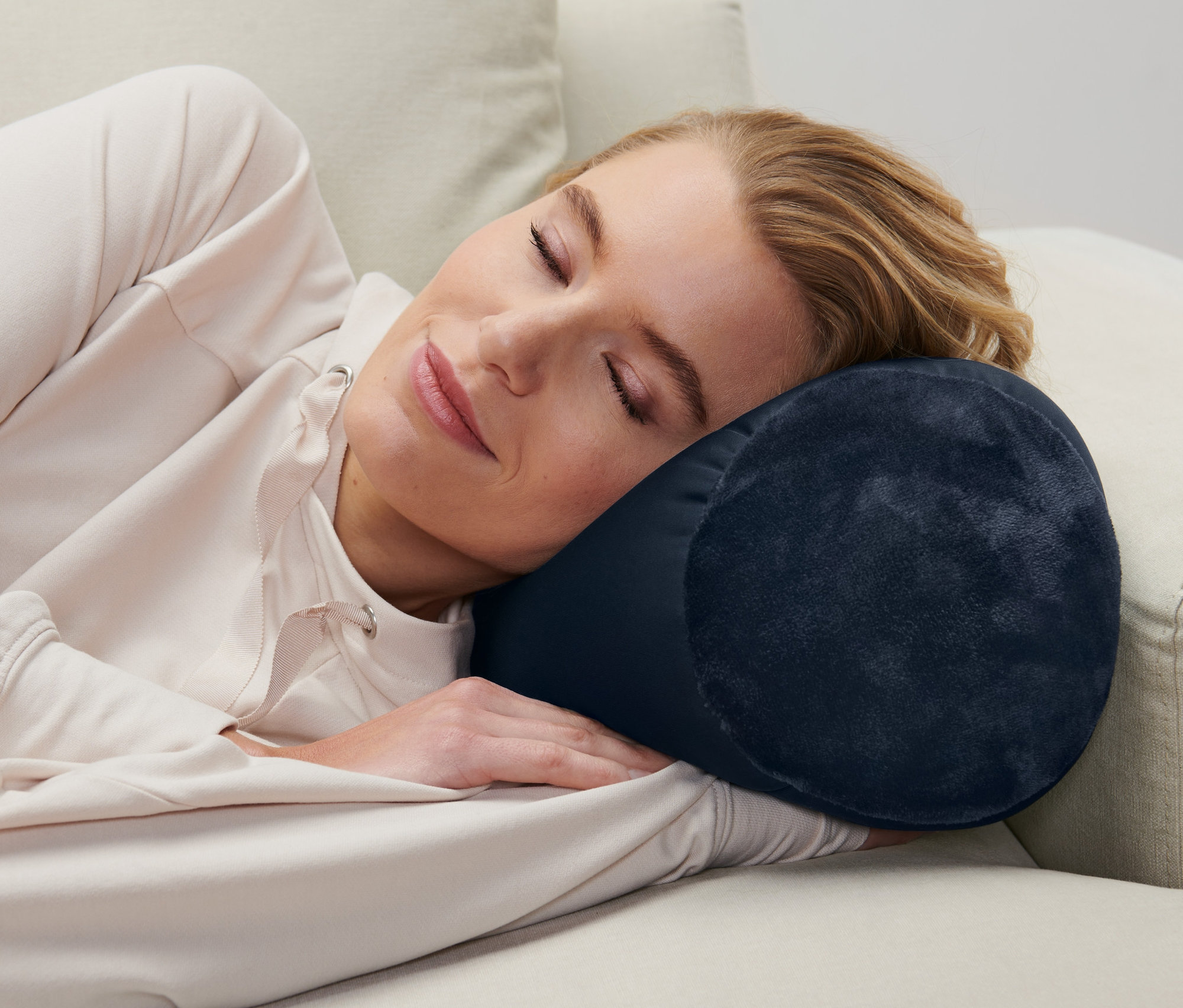 Frau liegt auf einer Couch und benutzt ein blaues Relaxkissen.