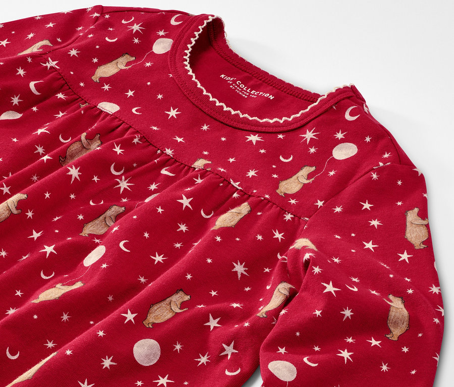 Detailaufnahme eines Kinder-Nachthemds mit Leggings. Das Nachthemd ist rot und mit Bären, Sternen und Monden bedruckt.