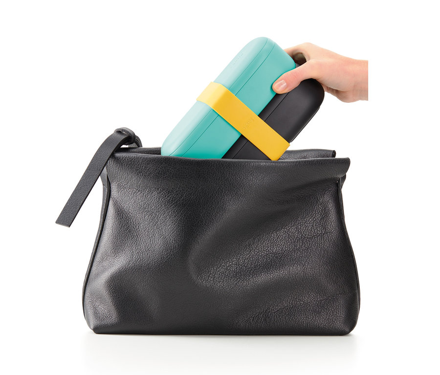 Eine Hand legt ein Lunch-Box-Set mit Besteck in eine schwarze Handtasche.