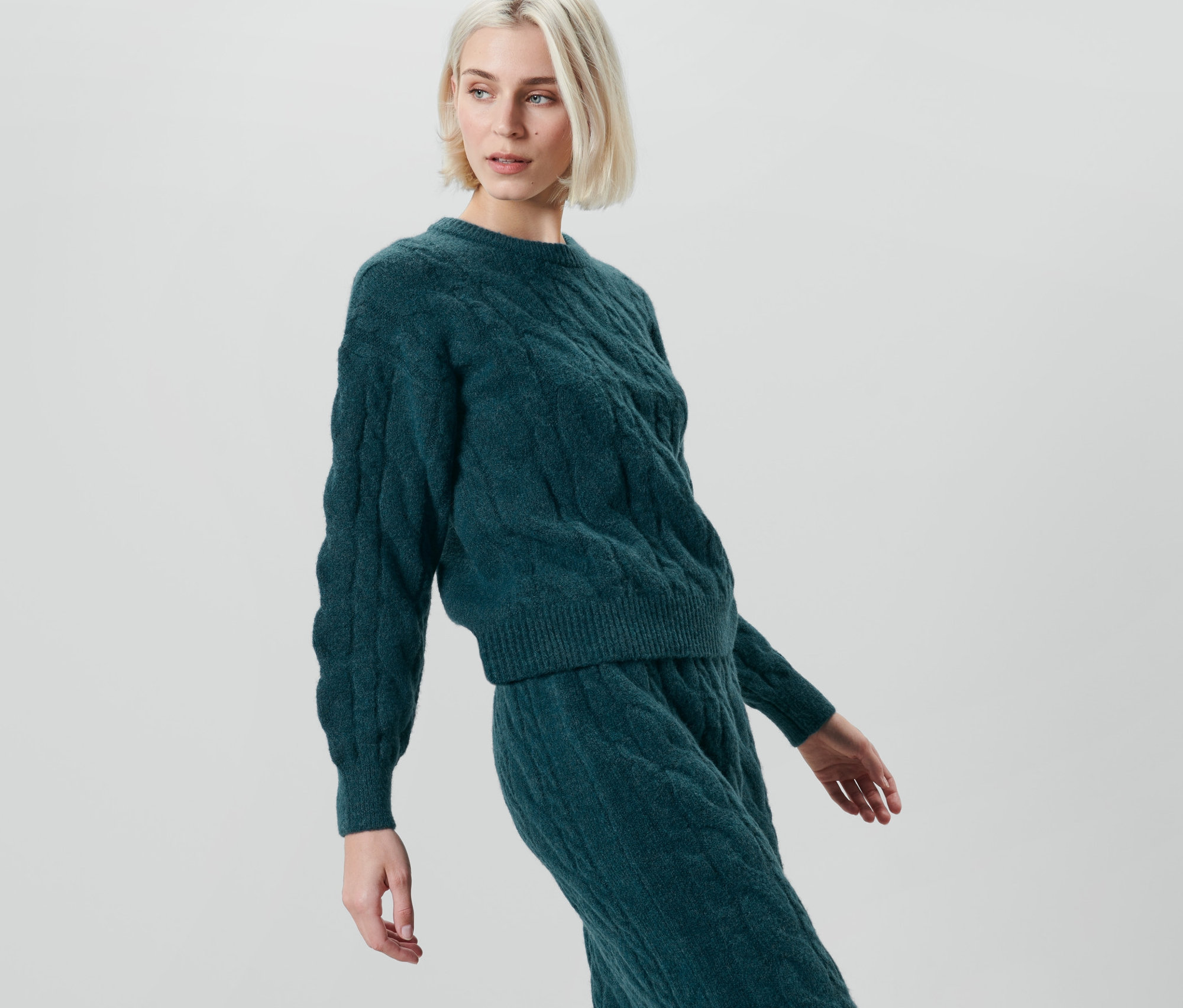 Frau posiert in einem petrolfarbenen Strickpullover.