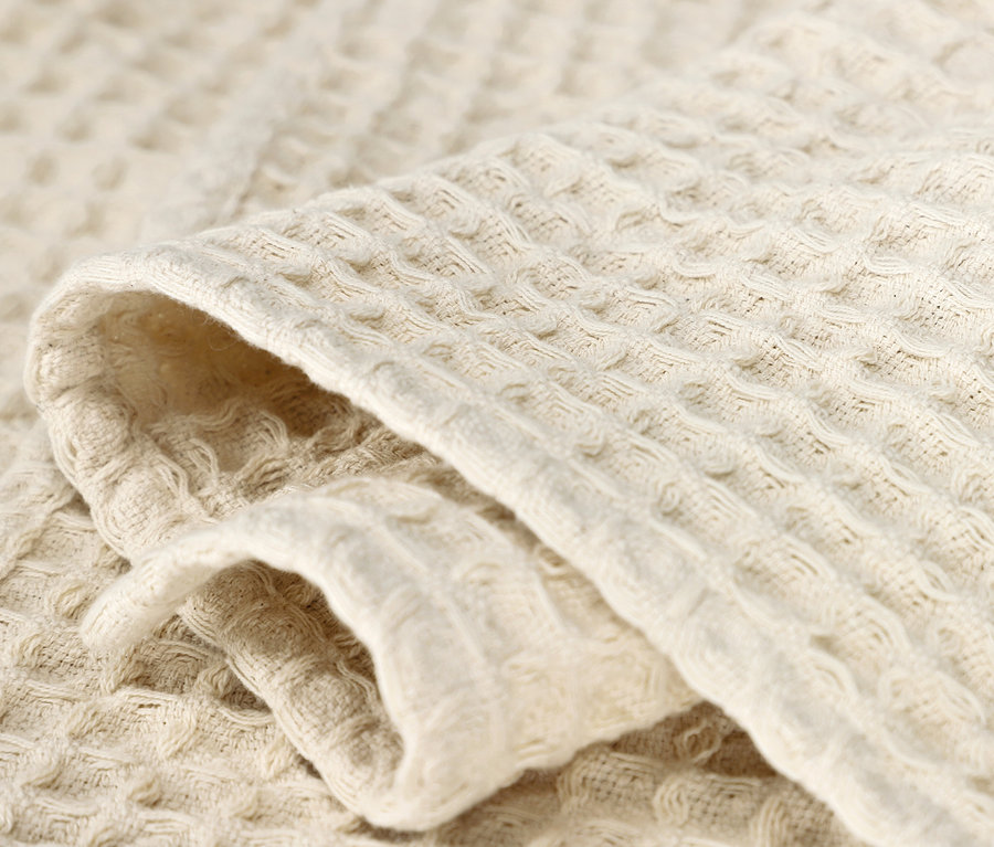 Detailaufnahme einer beigen Wohndecke mit Waffelstruktur.