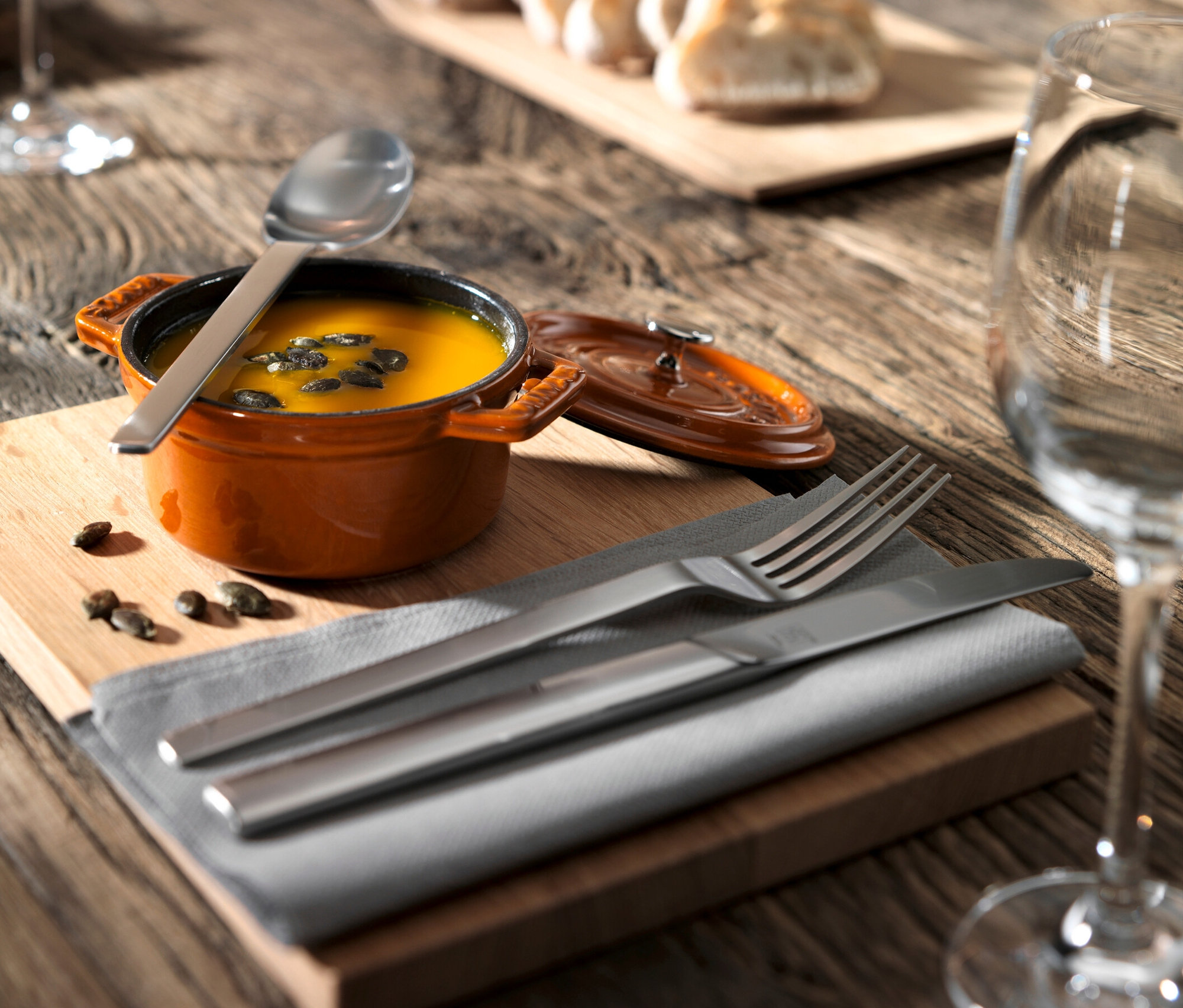Orangefarbene Suppe mit Kürbiskernen im Topf auf Holztisch mit Serviette und ZWILLING Besteck, mattiert, 60-teilig.