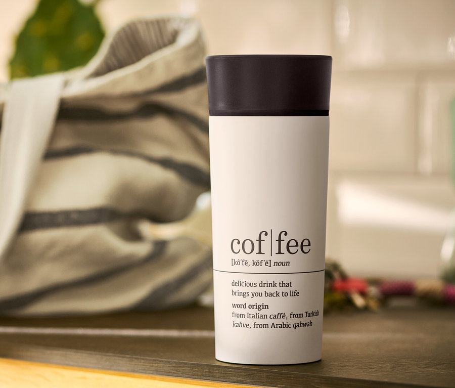 Weißer Coffee-to-go-Becher Coffee Dictionary mit schwarzem Deckel auf einem Tisch.