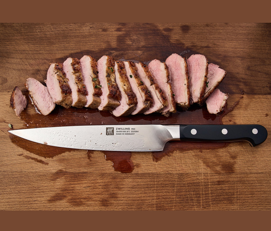Auf einem Holzbrett liegt aufgeschnittenes Fleisch neben einem ZWILLING PRO Messer.