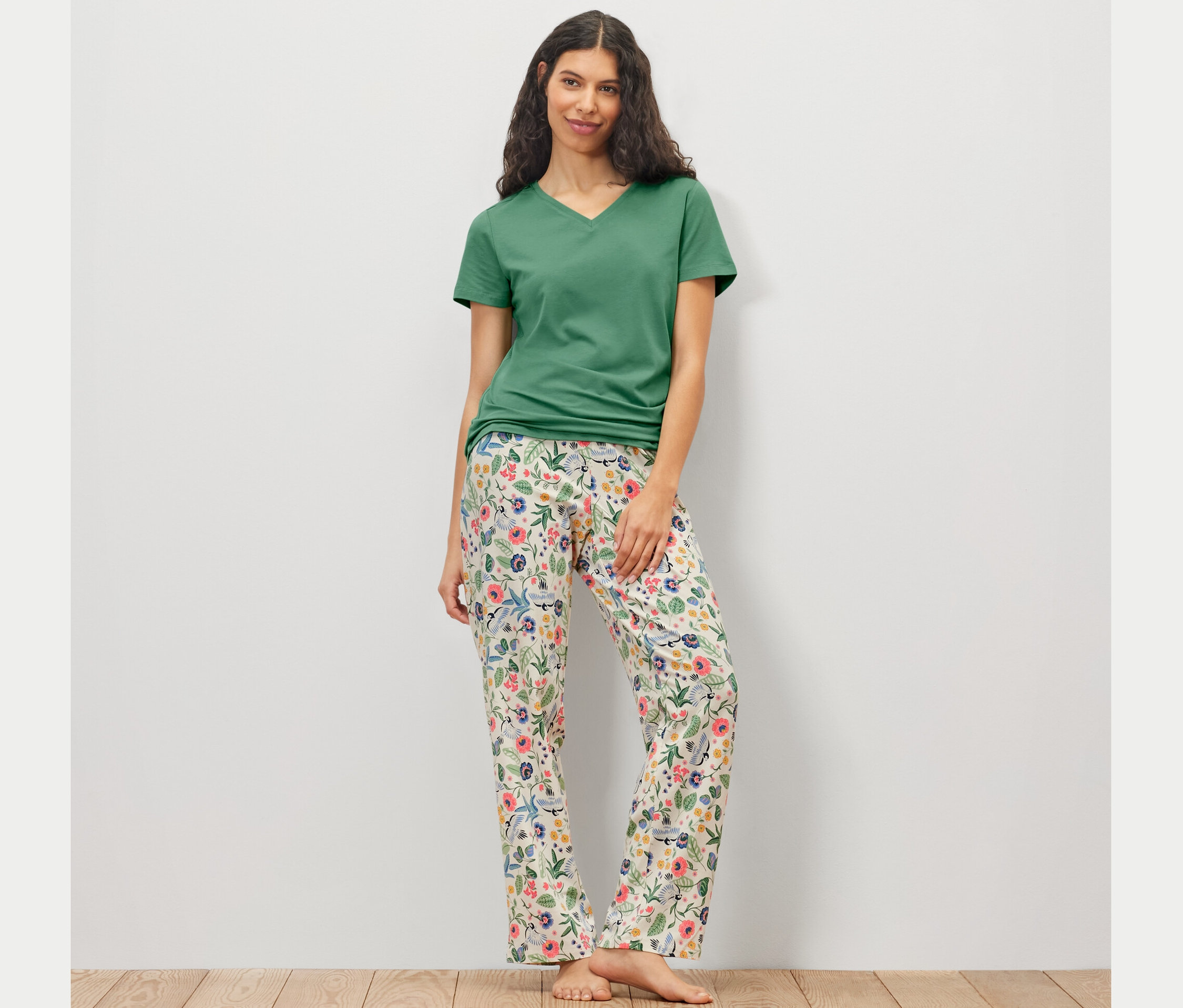 Frau trägt ein Pyjama-Set mit einer geblümten Hose und einem grünen T-Shirt.
