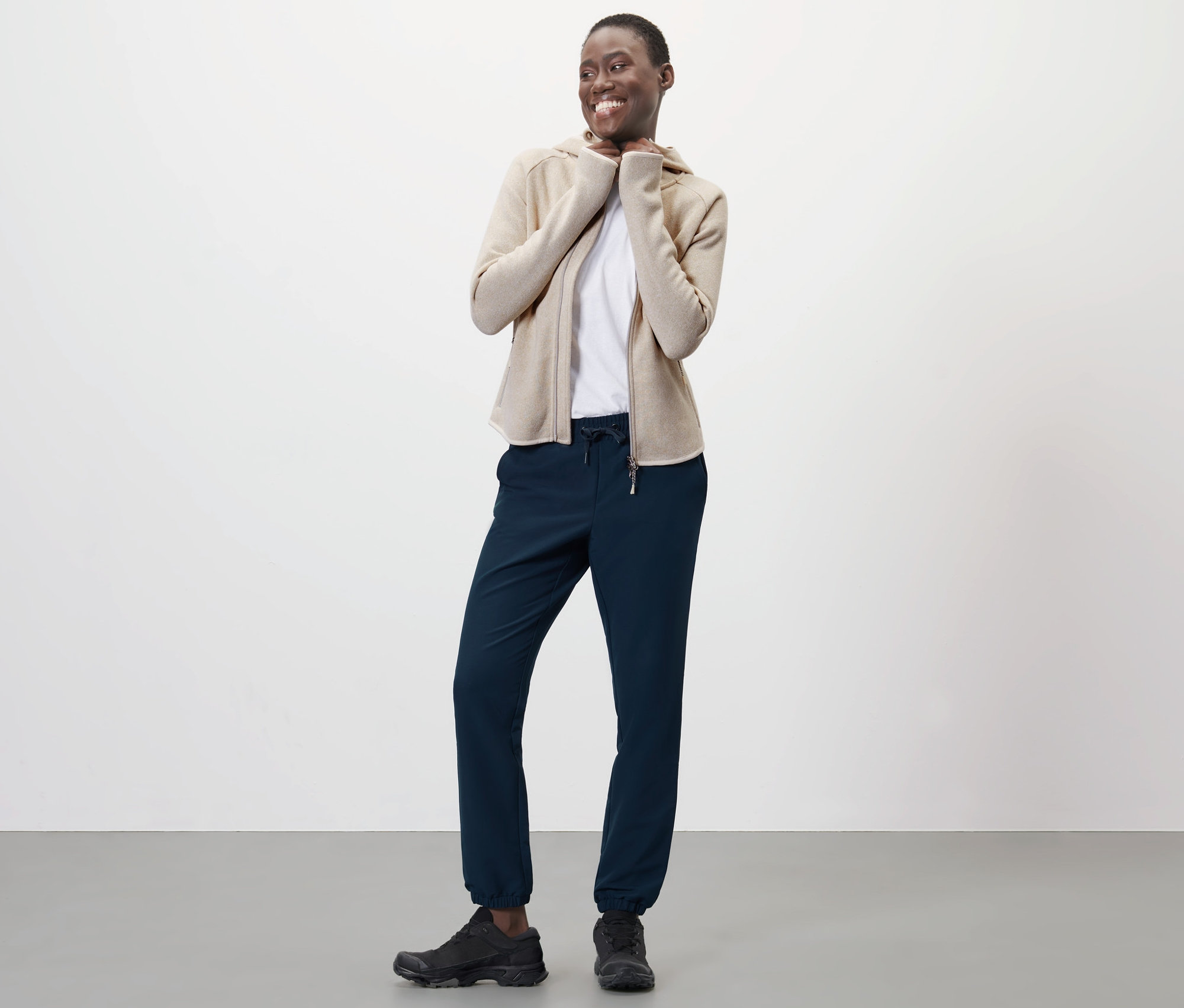 Frau trägt Softshell-Joggpants, eine Strickjacke mit Reißverschluss und Turnschuhe.