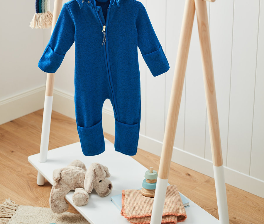 Blauer Strickfleece-Einteiler mit Kapuze mit recyceltem Material hängt auf einem Holzständer.