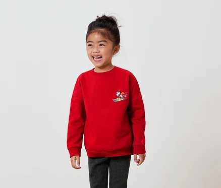 Lächelndes Mädchen trägt ein rotes Sweatshirt mit einer Cartoon-Figur auf der Brust.