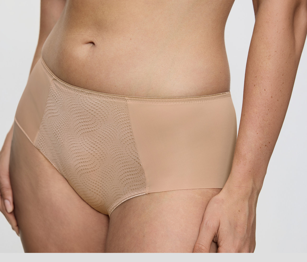 Nahaufnahme des Oberkörpers einer Person, die hautfarbene Triumph Essential »Minimizer Hipster X« Hüfthose trägt, mit glattem Stoff an den Seiten und einem strukturierten Mesh-Einsatz vorne.