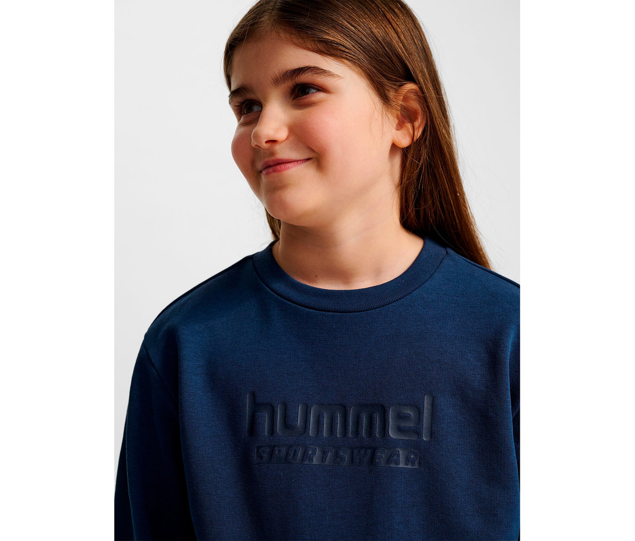 Porträt eines Mädchens mit langen braunen Haaren in blauem HUMMEL HMLJR Base-Sweatshirt.