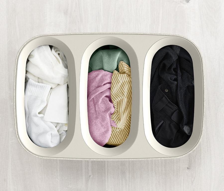 Draufsicht auf einen Wäschekorb mit drei Fächern, die mit verschiedenfarbiger Kleidung gefüllt sind.