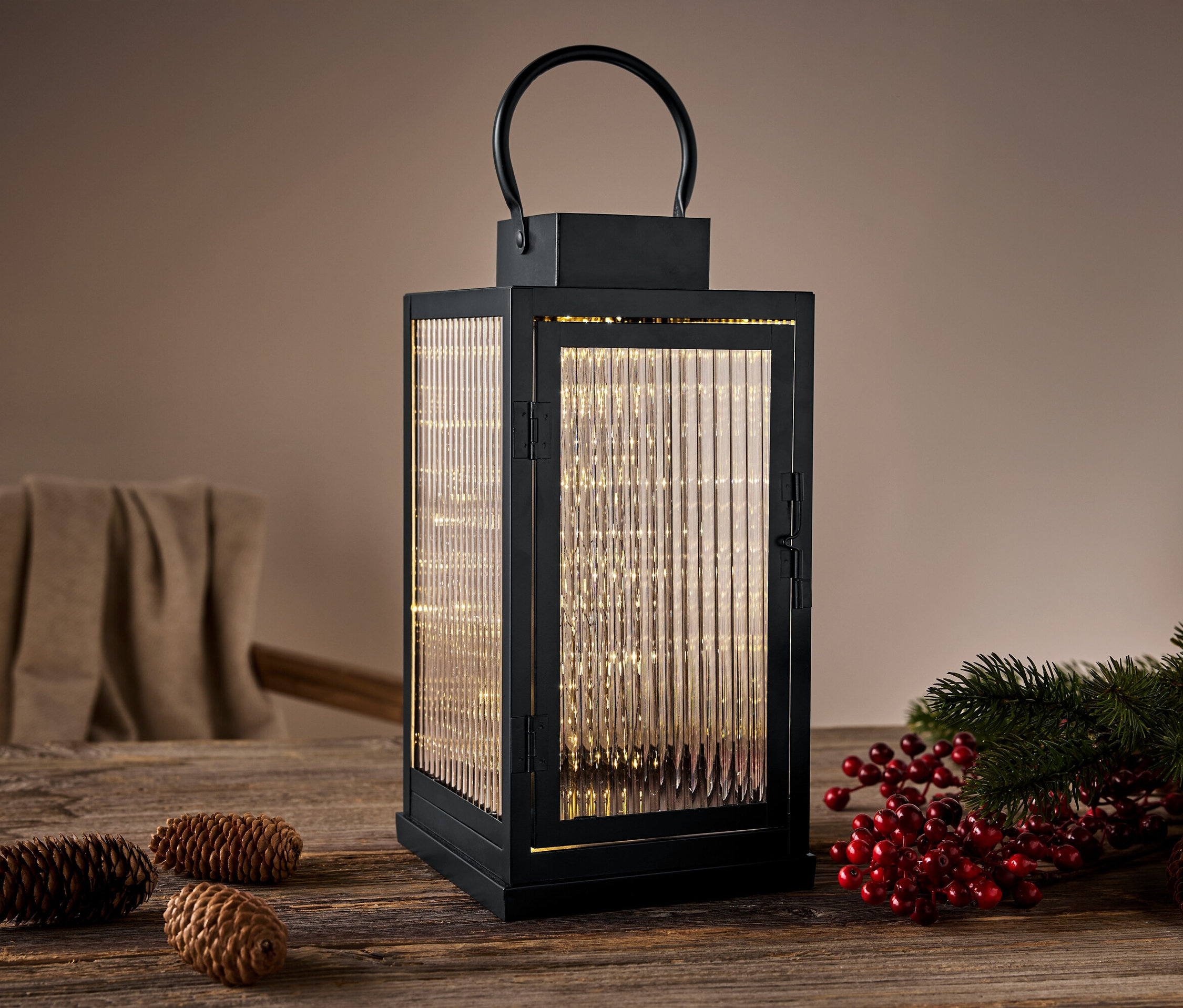 Schwarze Laterne mit Lichtern auf einem Holztisch mit Tannenzapfen und roten Beeren.