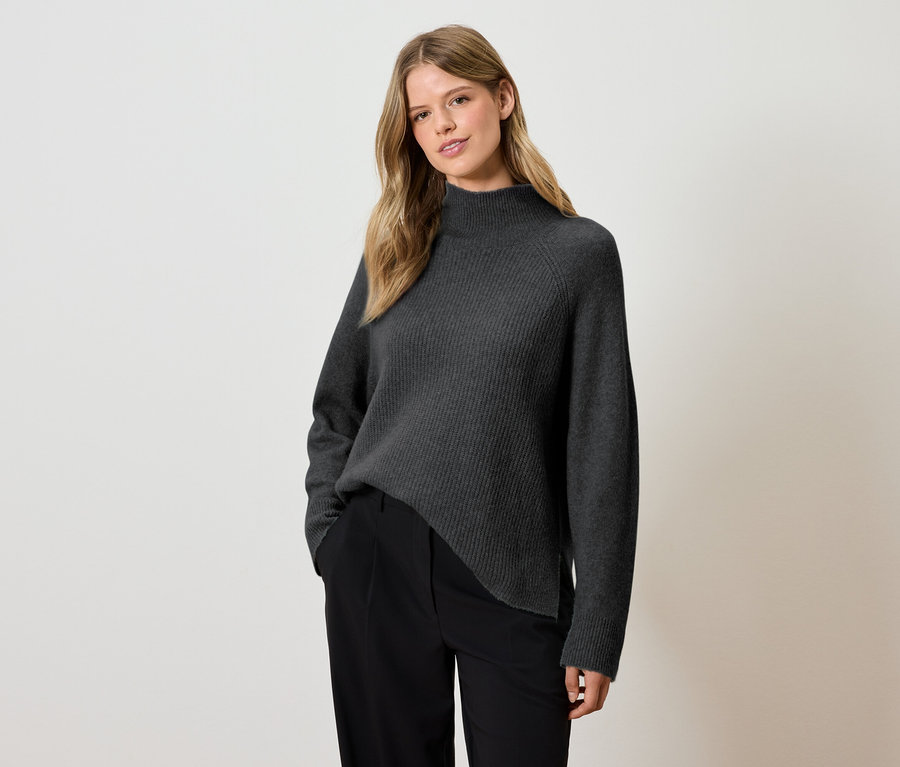 Frau posiert in einem grauen Rollkragenpullover und einer schwarzen Hose.