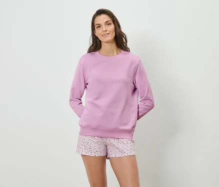 Frau trägt ein lila Sweatshirt und gemusterte Shorts.